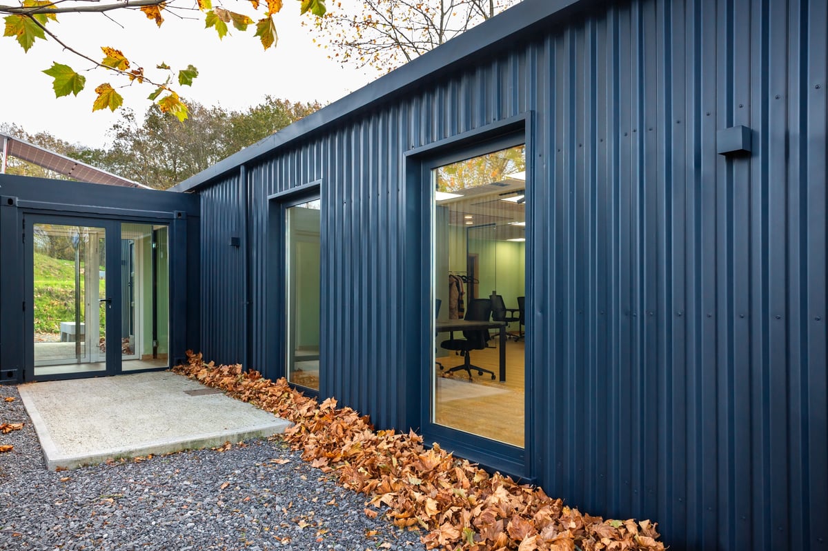 Entrance of a contemporary office building built from shipping containers with corrugated metal facade and large windows