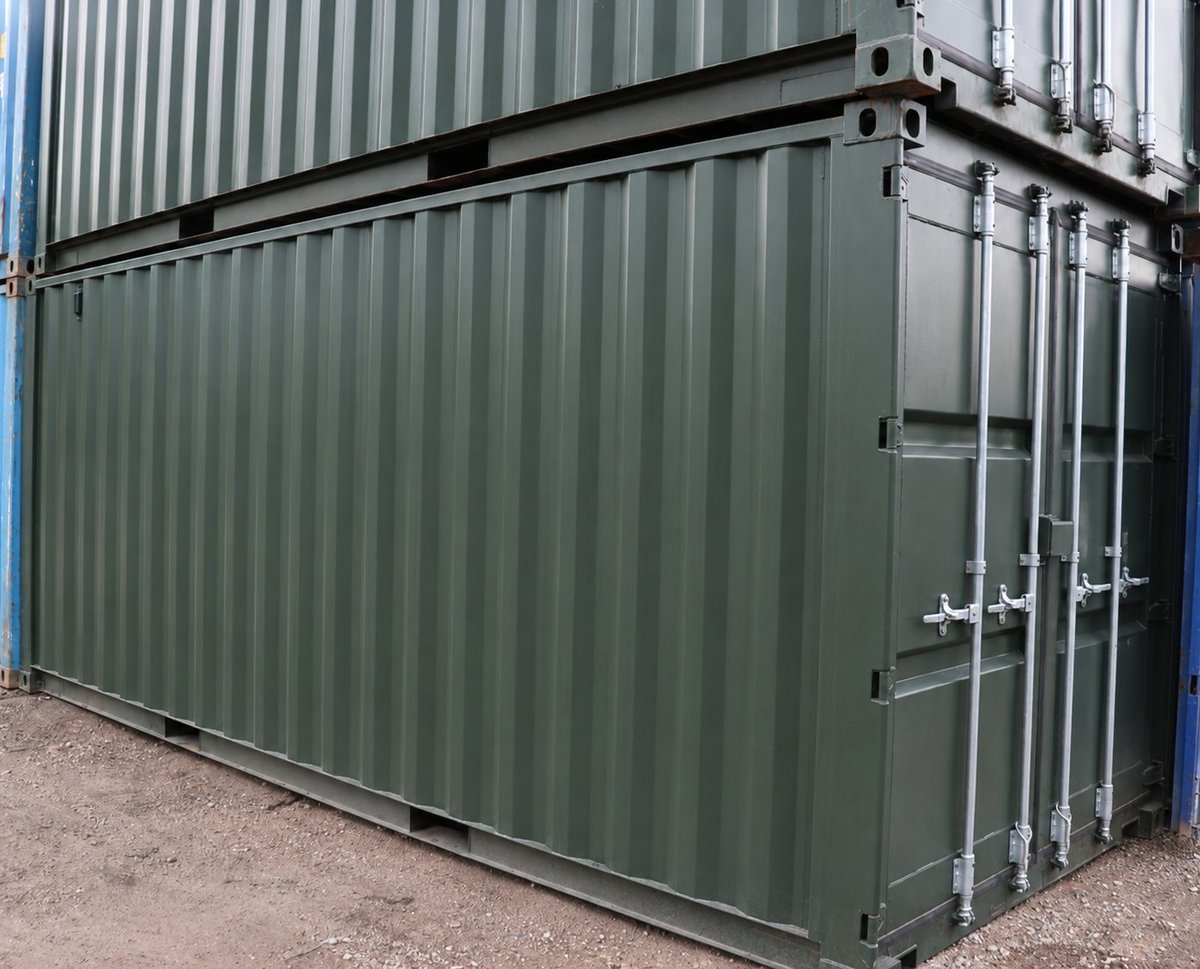 Green metal shipping container with corrugated walls and securing handles on paved ground