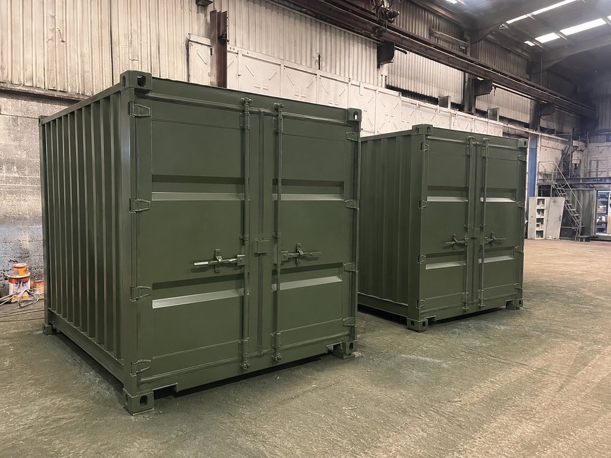 Two olive green shipping containers with double doors inside an industrial warehouse facility