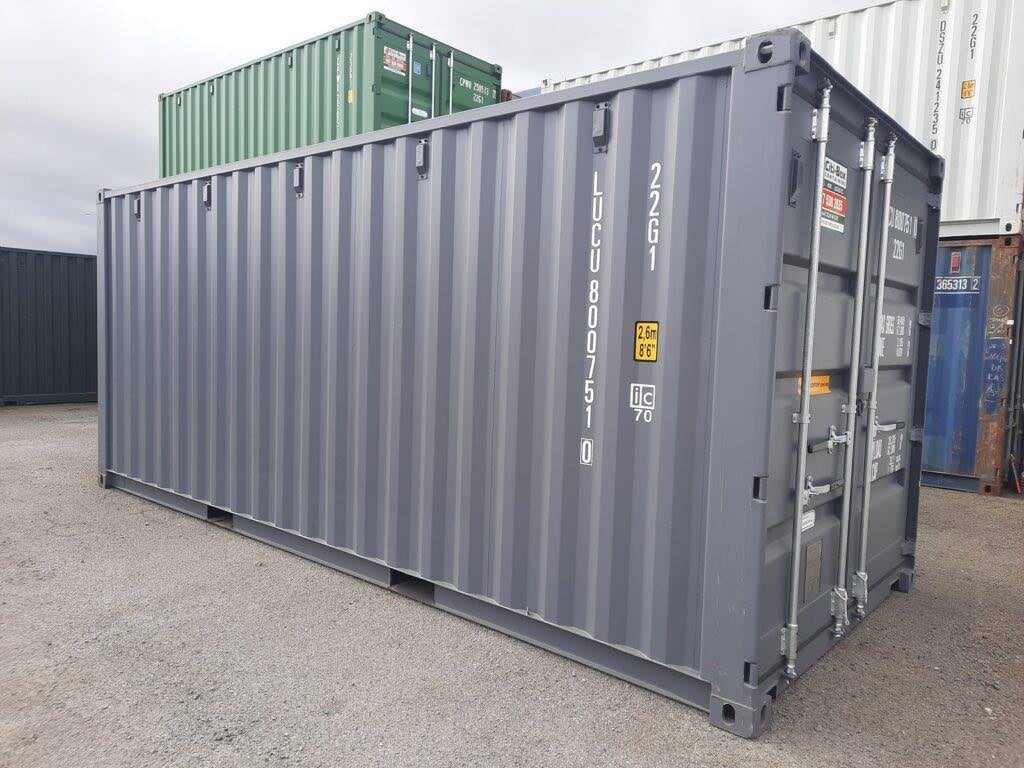 Grey 20ft shipping container with a stacked green container above in an industrial yard