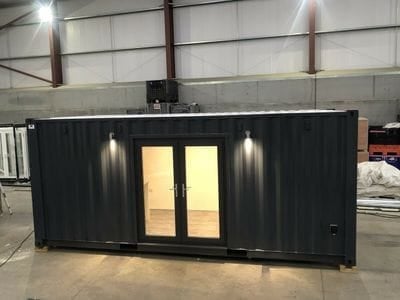 Black container structure with illuminated glass doors and side lights in an industrial warehouse setting