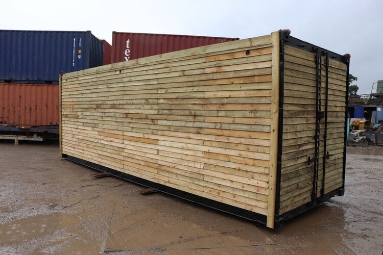 Wooden shipping container with metal frame and doors in a storage yard with stacked containers behind