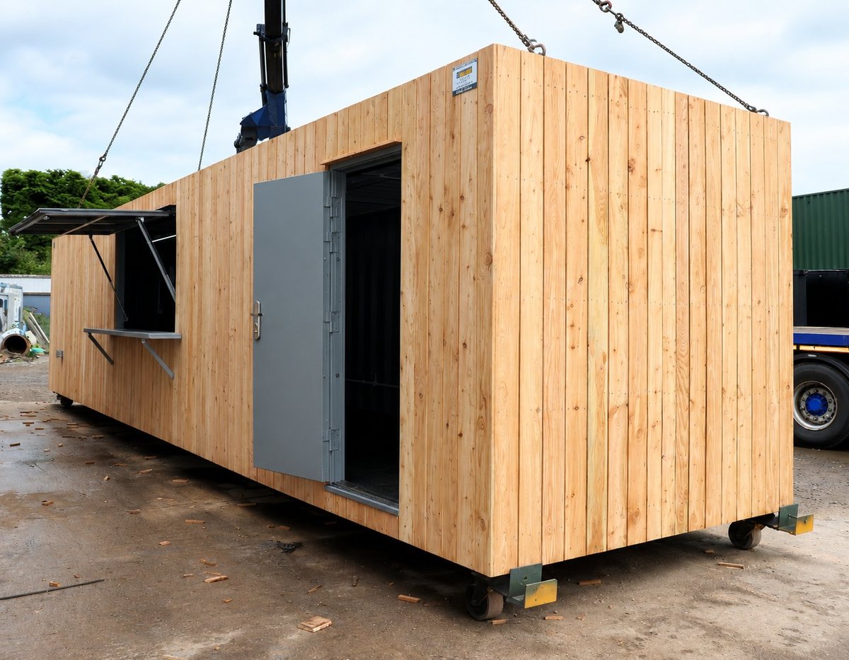 Timber-clad 40ft mobile office container with grey personnel door, mounted on castors and being lifted by chains